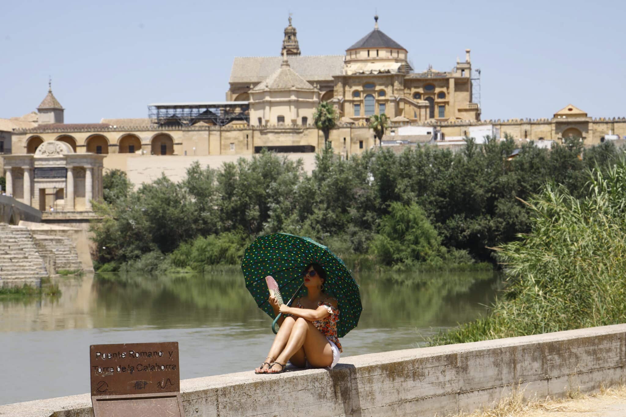 Una turista se protege del calor con un paraguas y un abanico a la orilla del río Guadalquivir