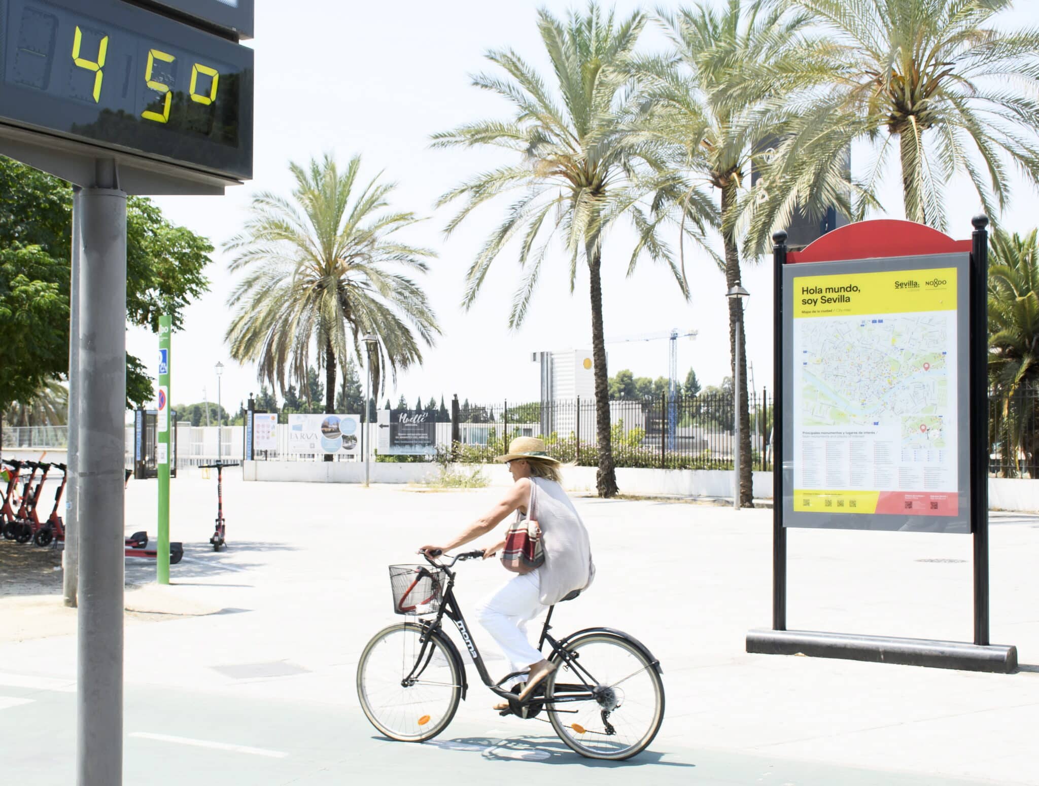 Una mujer en bicicleta pasa junto a un termómetro de calle en Sevilla que marca 45 grados