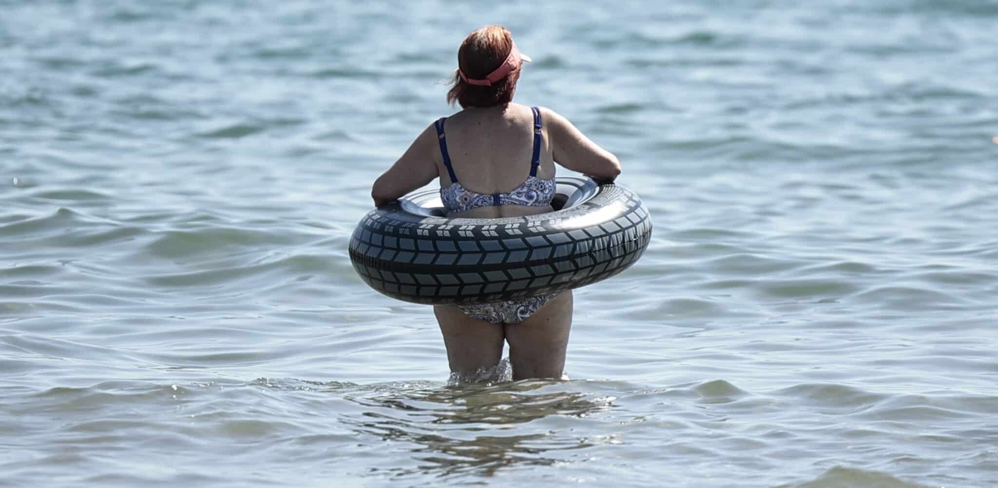 Una mujer se mete en el agua en la playa con un flotador