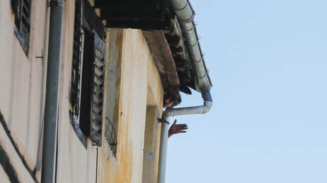 El hombre (c) que se ha atrincherado en su piso en el Casco Viejo de Vitoria saca la cabeza por la ventana mientras que la Ertzaintza ha desalojado el edificio por precaución