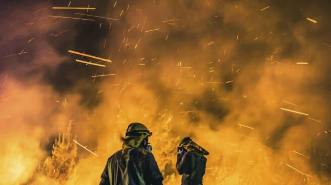 Operarios de las Brigadas de Refuerzo de Incendios Forestales (BRIF) lucha contra las llamas en la madrugada de este sábado para extinguir el incendio declarado en el día anterior en la parroquia de Cures, Boiro, A Coruña