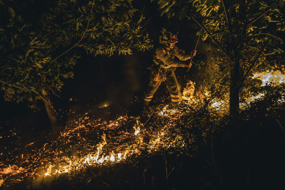 Un operario de las Brigadas de Refuerzo de Incendios Forestales (BRIF) lucha contra las llamas en la madrugada de este sábado para extinguir el incendio declarado en el día anterior en la parroquia de Cures, Boiro, A Coruña.