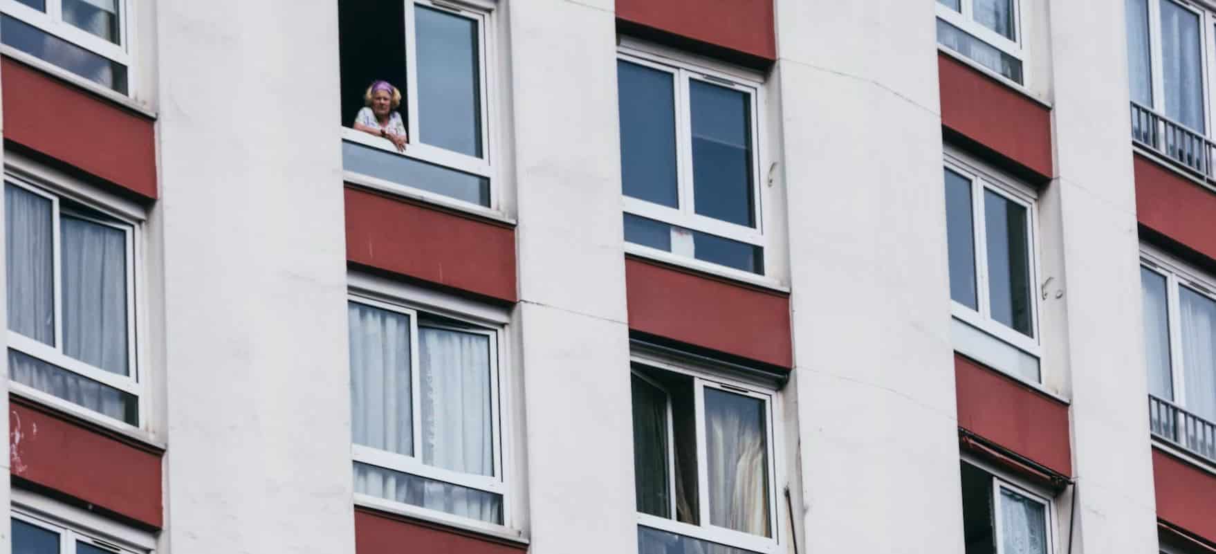 Una mujer asomada al balcón en un gran bloque de pisos.