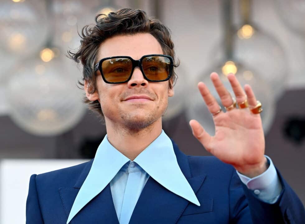Harry Styles, cantante y actor protagonista en Don't Worry Darling, en el Festival de Venecia 2022, con un traje azul y unas gafas de sol grandes, saludando a los fans y prensa