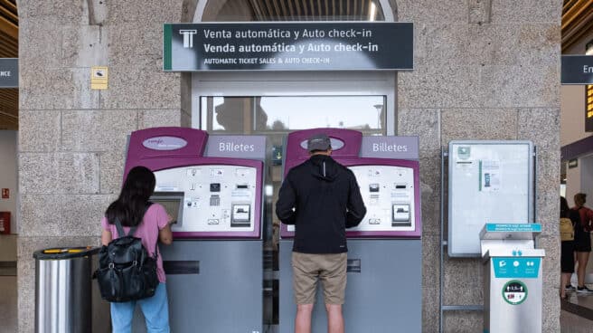 Dos personas compran billetes en los cajeros de venta automática en la estación de trenes en Santiago de Compostela