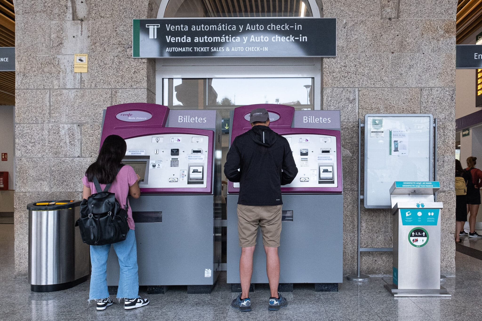 Dos personas compran billetes en los cajeros de venta automática en la estación de trenes en Santiago de Compostela