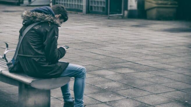 Un adolescente sentado en un banco de espaldas, posible víctima de acoso escolar.