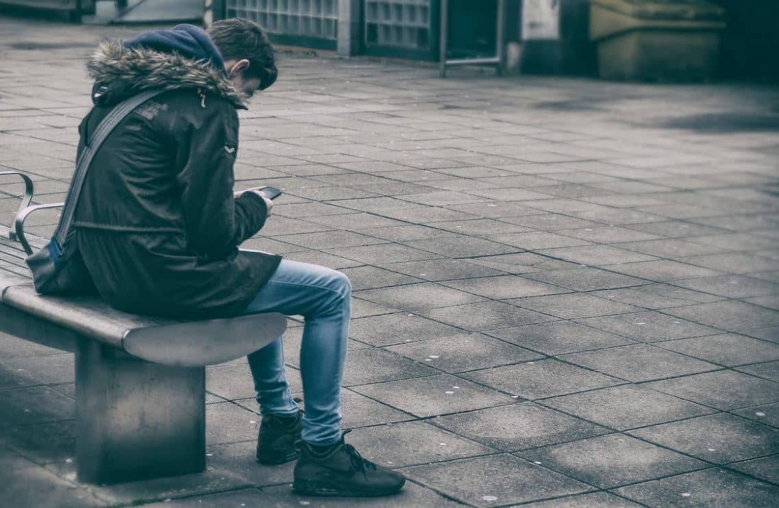 Un adolescente sentado en un banco de espaldas, posible víctima de acoso escolar.