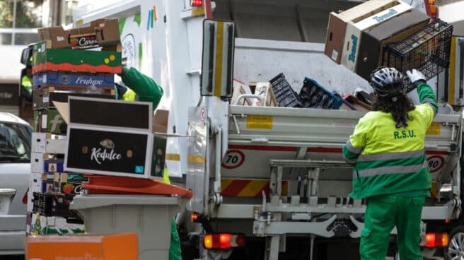 Un operario de recogida de residuos coloca cajas de cartón y de plástico en la trituradora de un camión de basura.