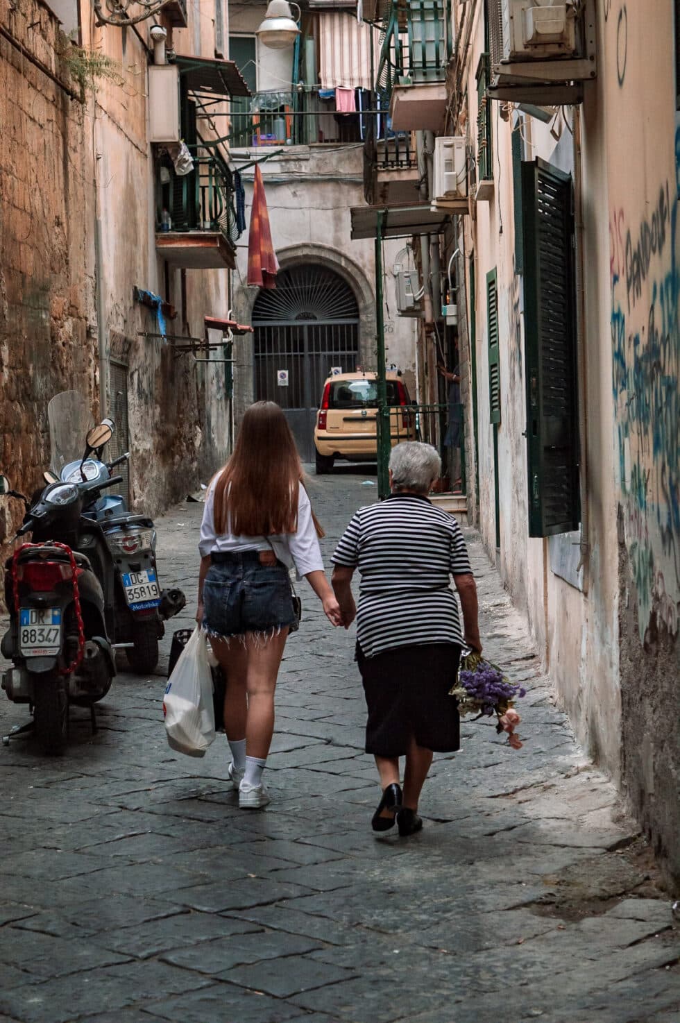 Una joven y su abuela pasean de la mano por el centro de Napolés