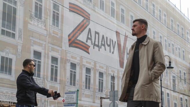 Dos hombres caminan frente a un cartel que reza 'La tarea será completada' en el centro de Moscú.