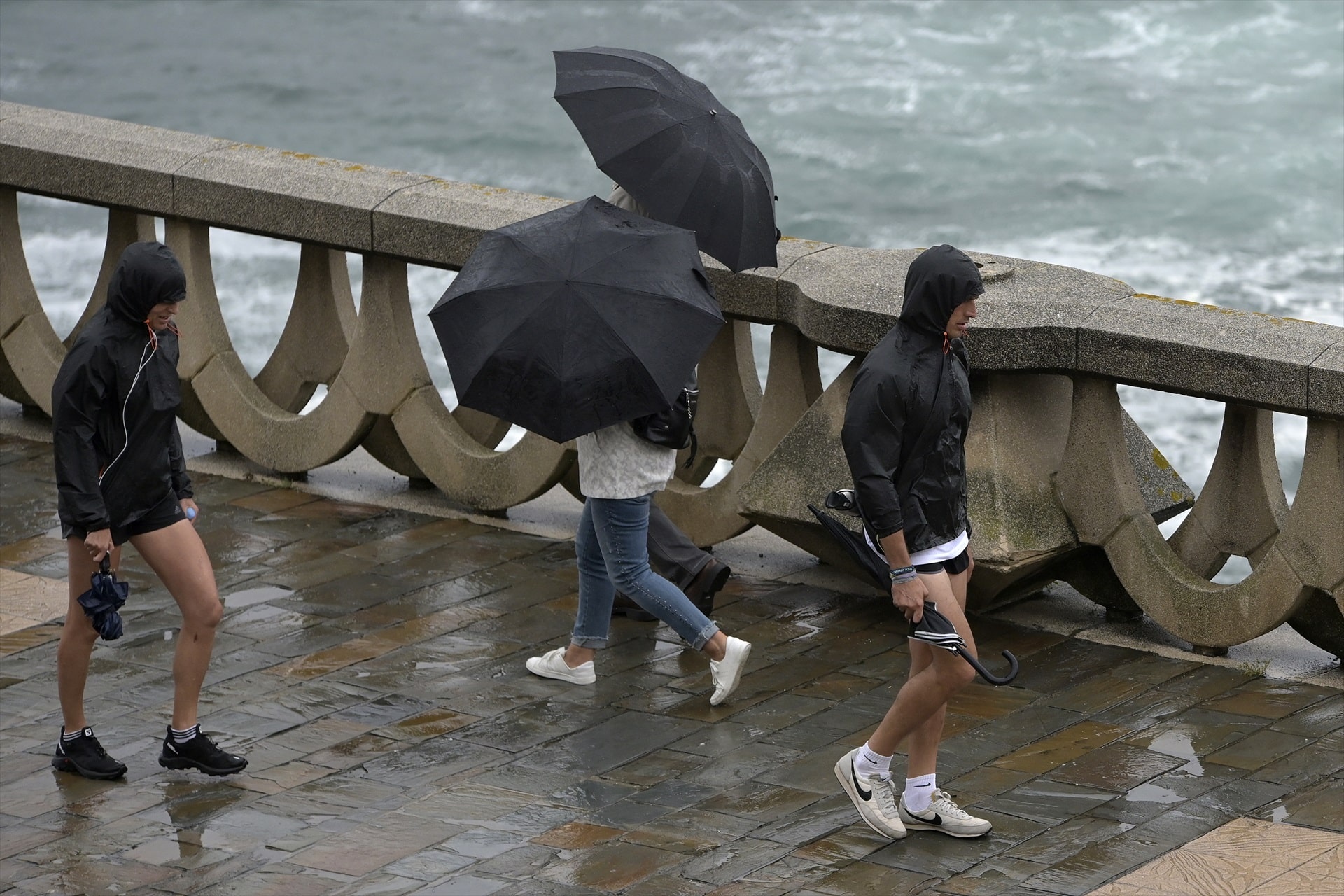 Gente caminando bajo la lluvia y el viento en el paseo marítimo de A Coruña