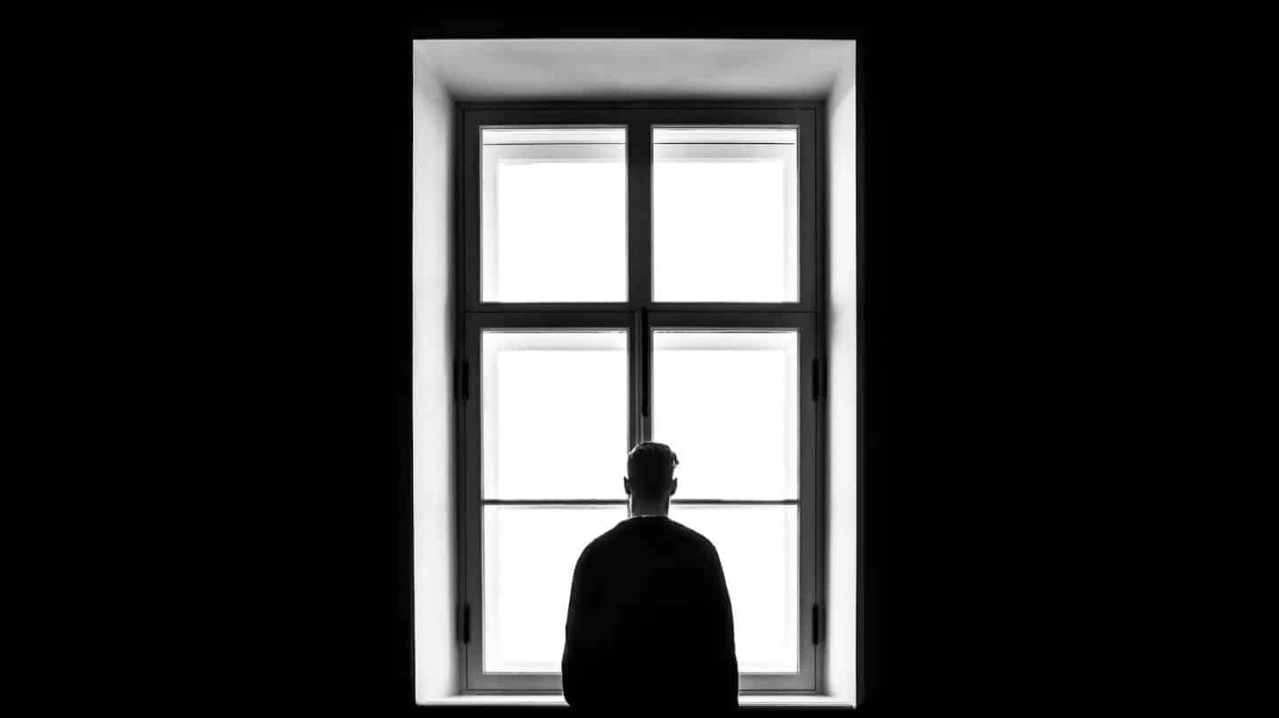 Una persona sola mira a través de una ventana en una imagen en blanco y negro.