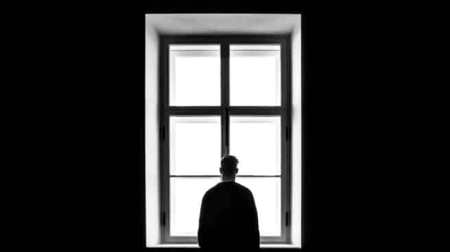 soledad-envejecimiento Una persona sola mira a través de una ventana en una imagen en blanco y negro.