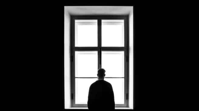 Una persona sola mira a través de una ventana en una imagen en blanco y negro.