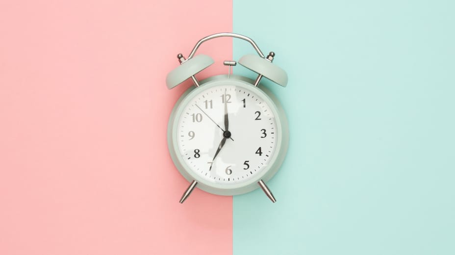 Reloj despertador que marca el cambio de hora sobre fondo rosa y azul turquesa