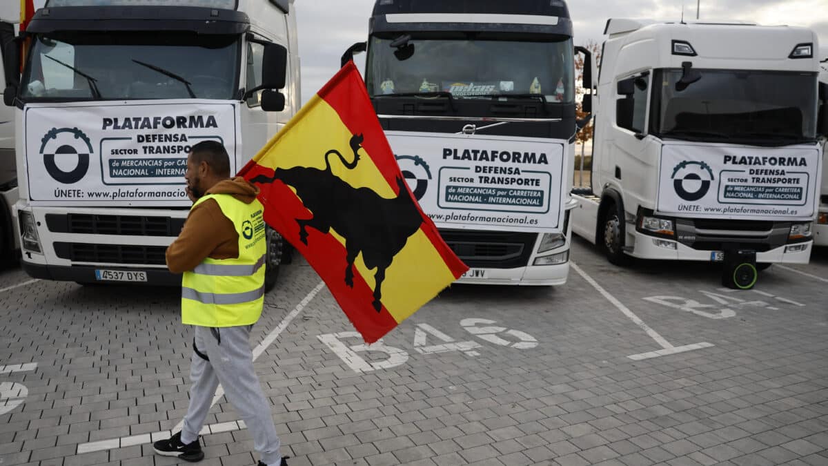 Un camionero porta una bandera frente a varios vehículos.