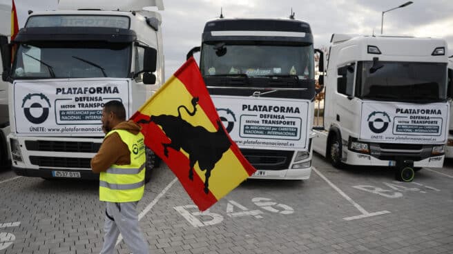 Un camionero porta una bandera frente a varios vehículos.