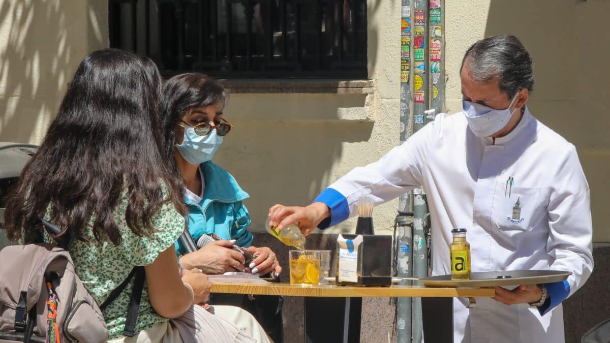 Un camarero sirve un refresco a dos personas en una terraza, en Madrid.