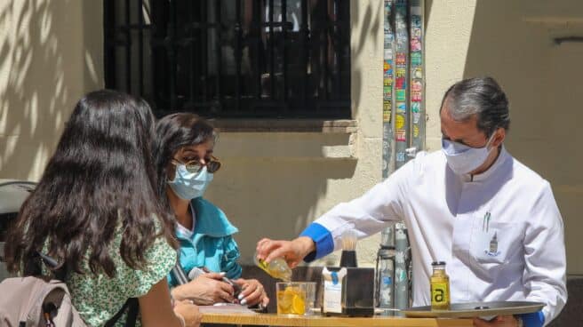 Un camarero sirve un refresco a dos personas en una terraza, en Madrid.