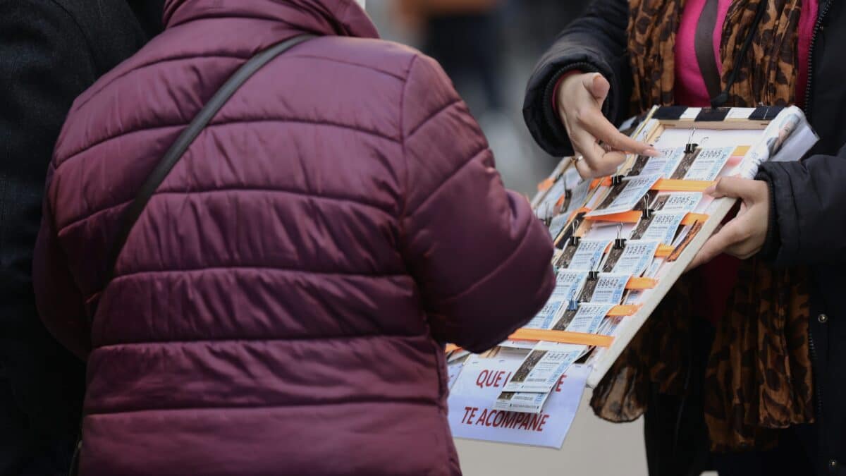 Una mujer compra un décimo de lotería a una vendedora ambulante, tres días antes del Sorteo de La Lotería del Niño