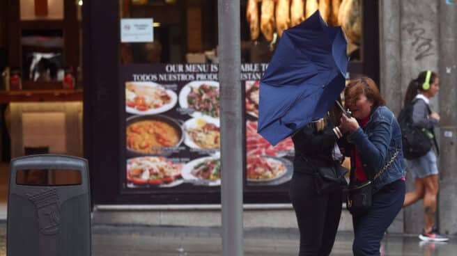 Dos chicas intentan controlar su paraguas, en la calle Gran Vía