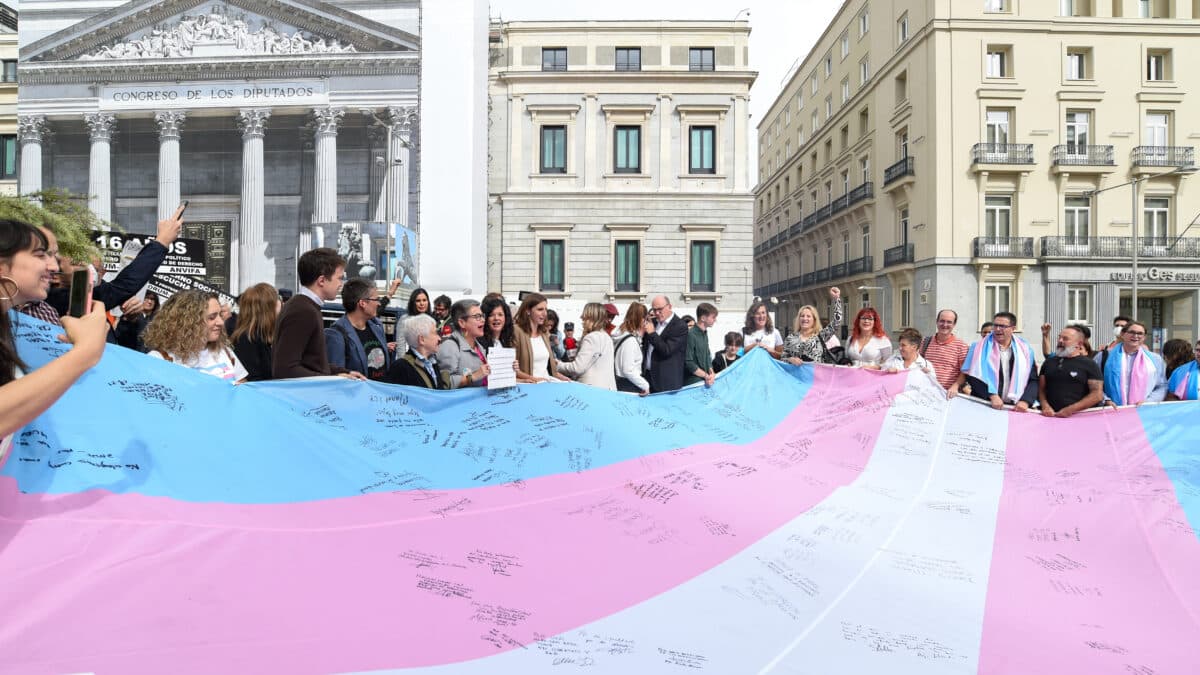 Varias personas sostienen la bandera trans que la Federación Estatal de Lesbianas, Gais, Trans, Bisexuales, Intersexuales y más (Flegtbi+), Chrysallis y Fundación Triángulo han llevado al Congreso de los Diputados, a 27 de octubre de 2022, en Madrid (España). El fin de llevar la bandera trans al Congreso es visibilizar su protesta ante los rechazos que sufre la tramitación de la conocida como ‘ley trans’ y exigir que el texto ‘’no sufra recortes’’. Los tres colectivos aprovechan su acto de protesta ante la Cámara Baja para reclamar a los representantes de los distintos grupos parlamentarios que firmen la bandera como muestra de su compromiso de “acelerar los trámites parlamentarios”. La acción tiene lugar en el marco del ‘Octubre trans’.