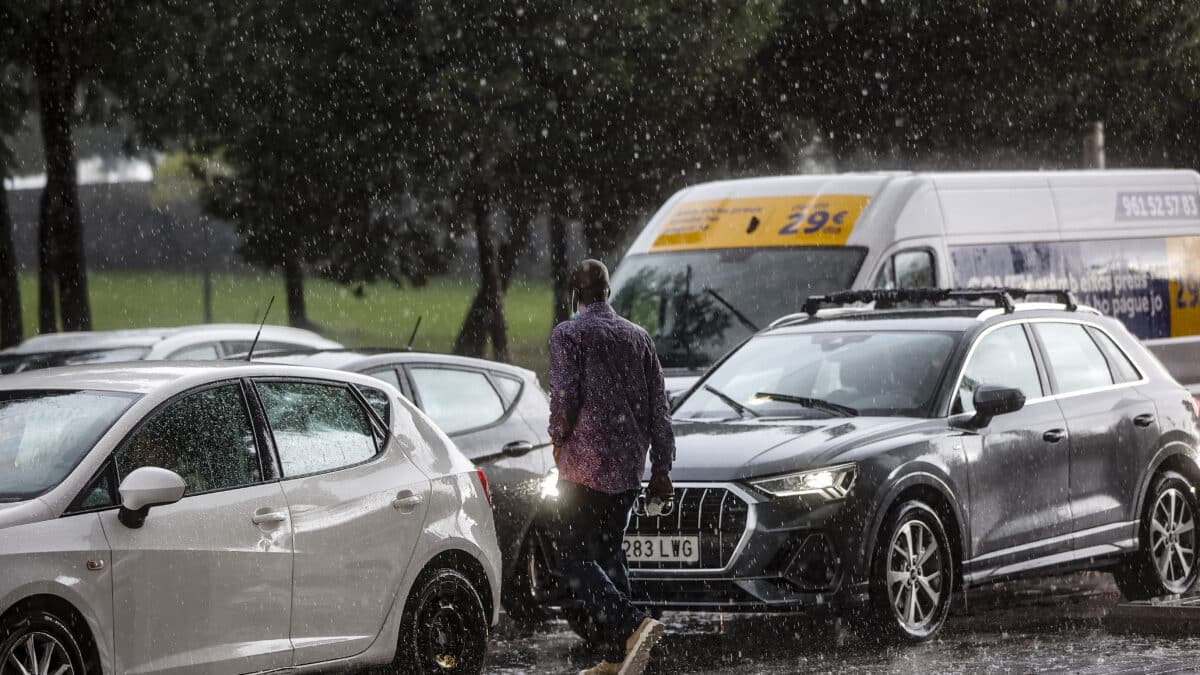 Un hombre camina entre varios coches mientras la lluvia cae