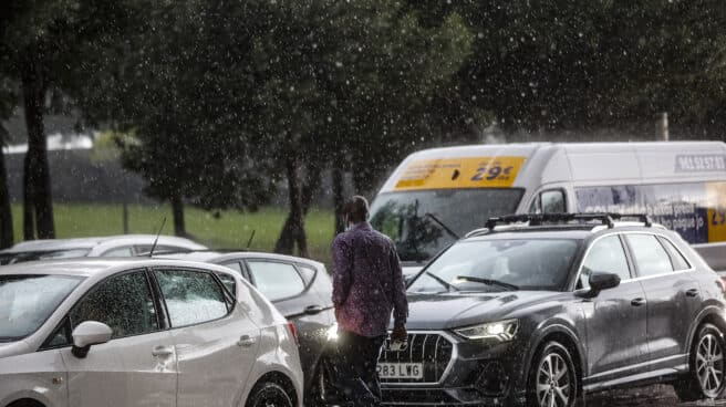 Un hombre camina entre varios coches mientras la lluvia cae