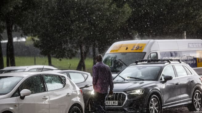 La DANA dejará inundaciones y dará paso a un nuevo "veranillo de San Miguel" Un hombre camina entre varios coches mientras la lluvia cae