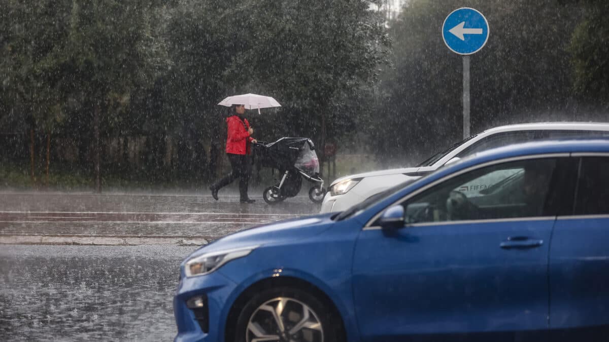 Una mujer lleva un carrito de bebé mientras se protege de la lluvia con un paraguas