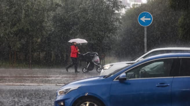 Una mujer lleva un carrito de bebé mientras se protege de la lluvia con un paraguas