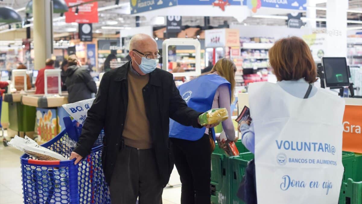 Un hombre entrega un paquete de pasta a una voluntaria en la recogida de comida y donativos de la Fundación Banco de Alimentos de Madrid, en un supermercado de la capital.