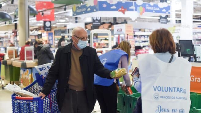 Un hombre entrega un paquete de pasta a una voluntaria en la recogida de comida y donativos de la Fundación Banco de Alimentos de Madrid, en un supermercado de la capital.