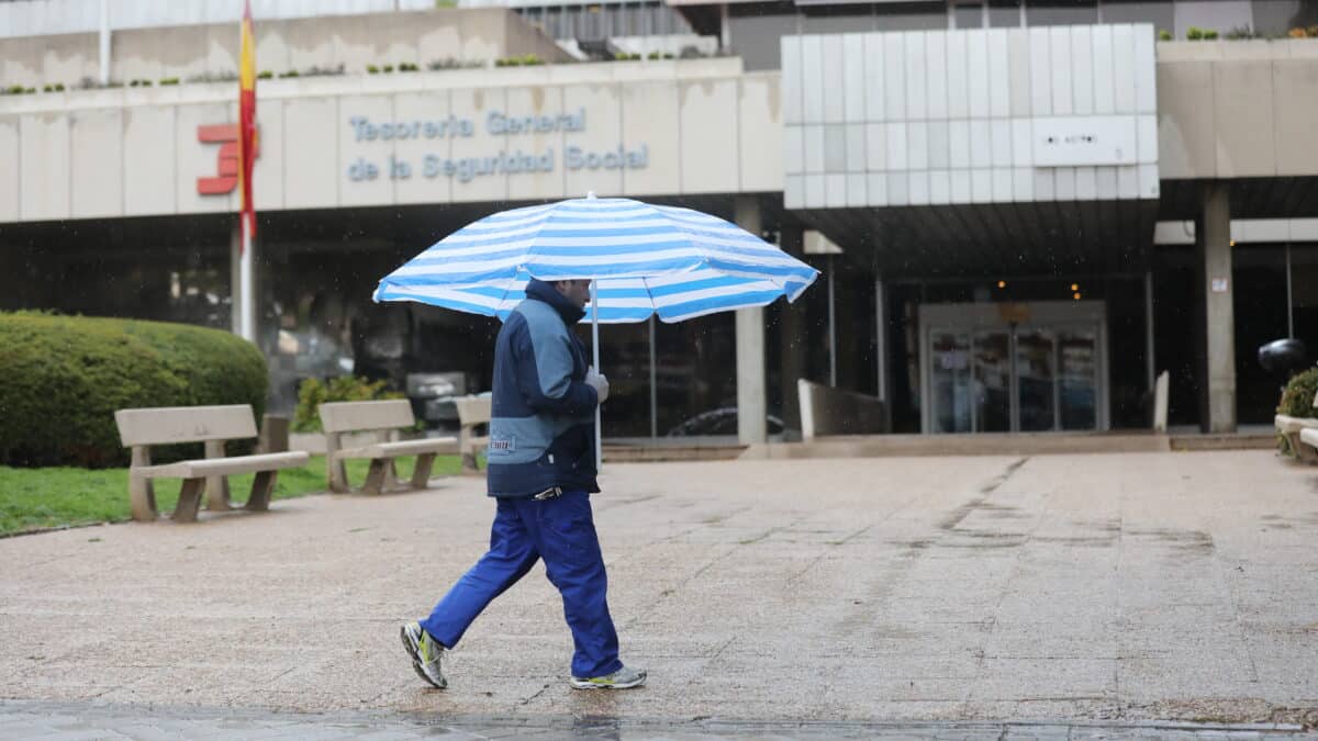 Un hombre con paraguas pasa frente a una oficina de la Tesorería General de la Seguridad Social en Madrid.