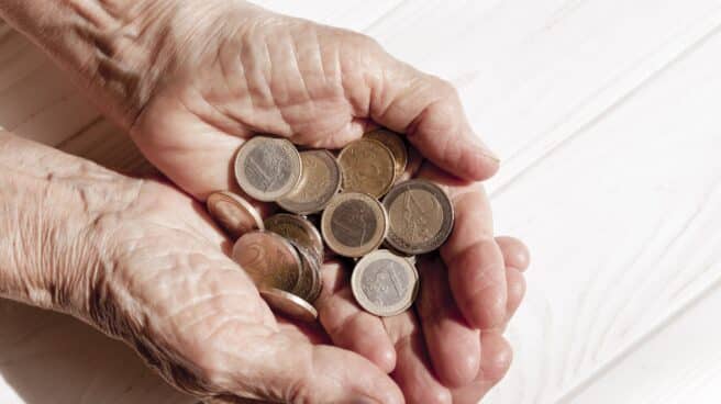 Una persona mayor sostiene monedas en sus manos.
