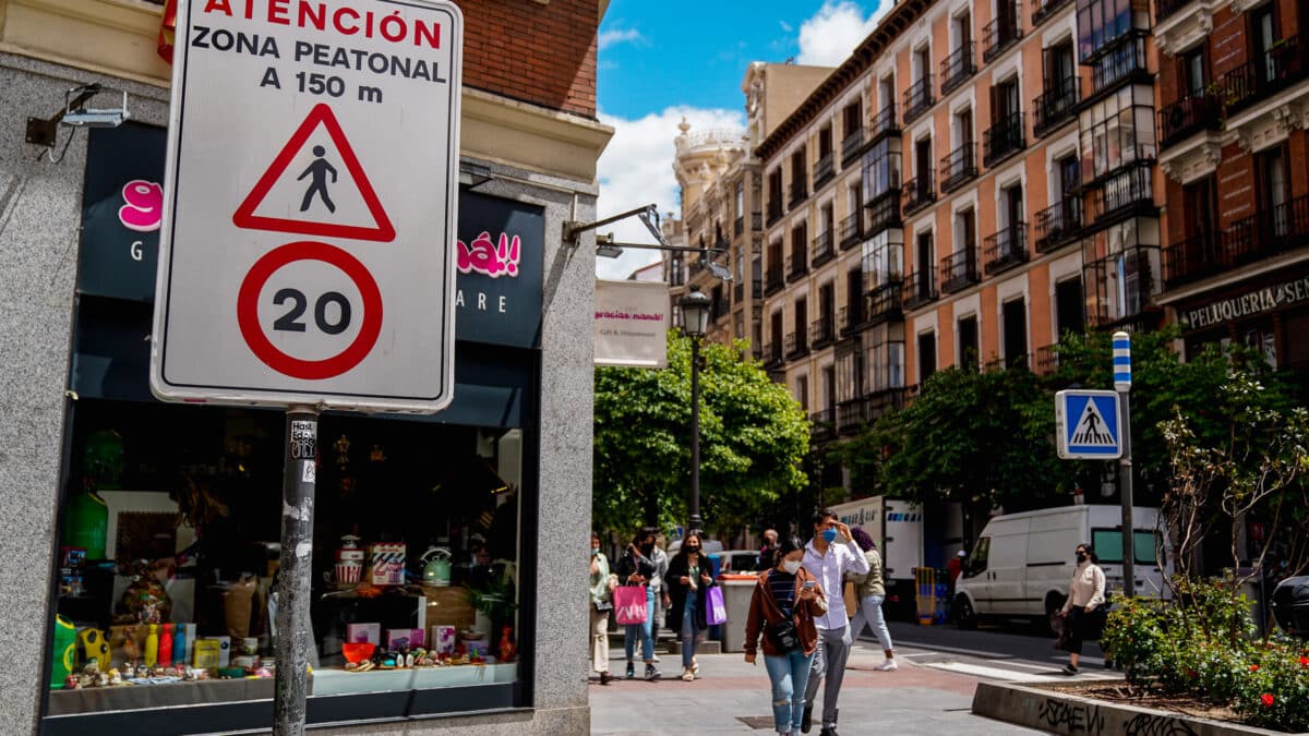Viandantes pasan al lado de una señal que indica la limitación de la circulación a 20 km/h en una calle de Madrid