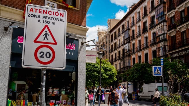 Viandantes pasan al lado de una señal que indica la limitación de la circulación a 20 km/h en una calle de Madrid