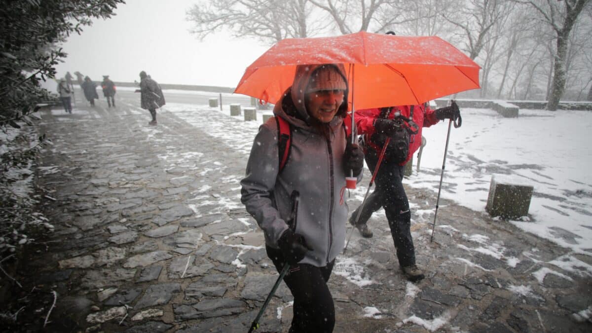 Una persona camina con bastones y ropa de abrigo mientras nieva en la parroquia de O Cebreiro