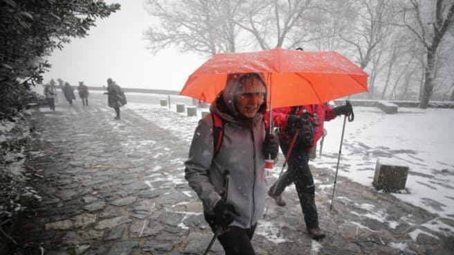 Una persona camina con bastones y ropa de abrigo mientras nieva en la parroquia de O Cebreiro