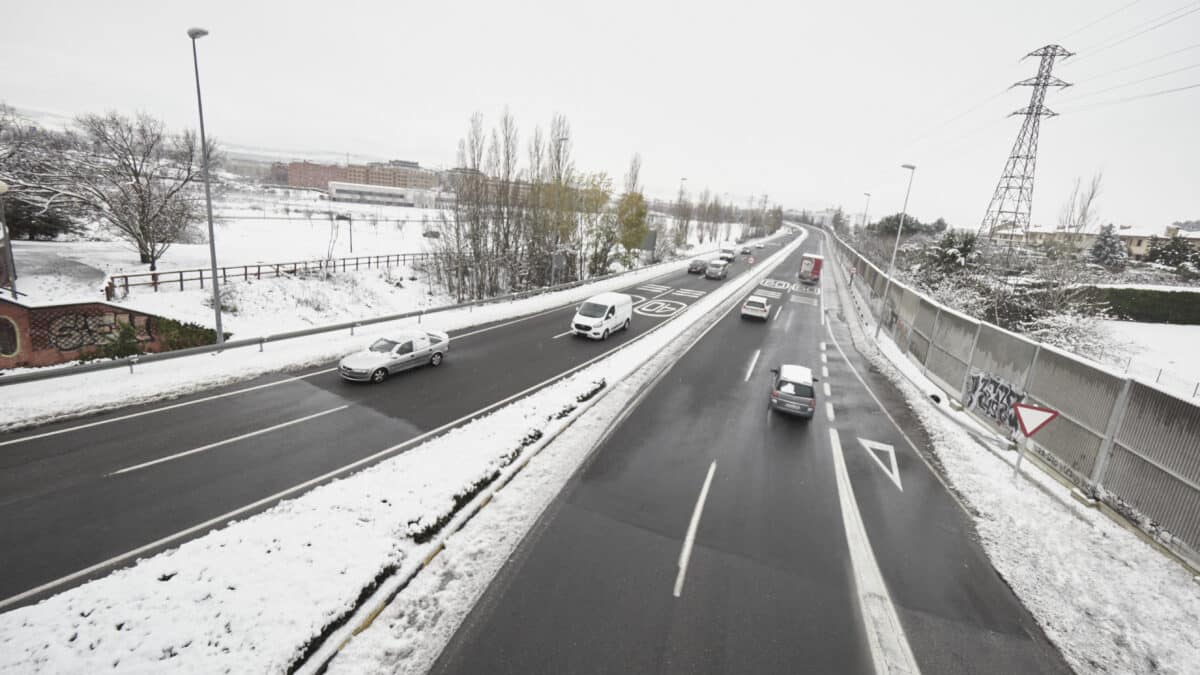 Varios coches circulan por una carretera con los laterales cubiertos de nieve