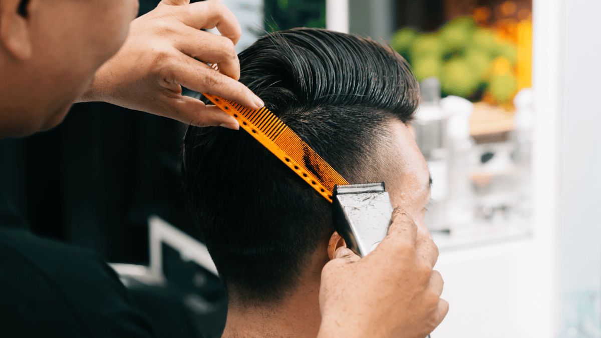 Hombre joven que se corta el pelo en una peluquería con maquinilla de afeitar, con la que se está transmitiendo los brotes de tiña