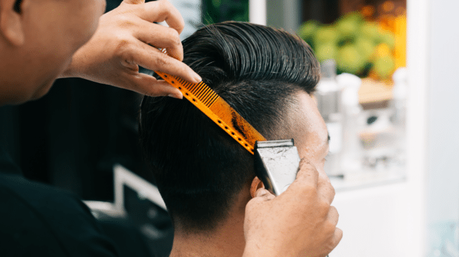 Hombre joven que se corta el pelo en una peluquería con maquinilla de afeitar, con la que se está transmitiendo los brotes de tiña