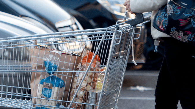 Mujer empujando un carro con bolsas de la compra en el aparcamiento de un supermercado, usando el cheque ayuda de 200 euros para la cesta de la compra del Gobierno.