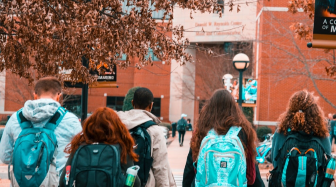 Grupo de cuatro estudiantes universitarios, en su campus, acudiendo a clase.