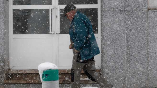 Hombre caminando con el tiempo frío de España en una calle cubierta de nieve en Pedrafita do Cebreiro, Lugo, Galicia