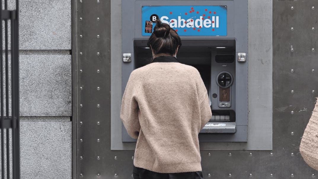 Mujer que va a cobrar la pensión en febrero 2023 frente a un cajero automático del Banco Sabadell.