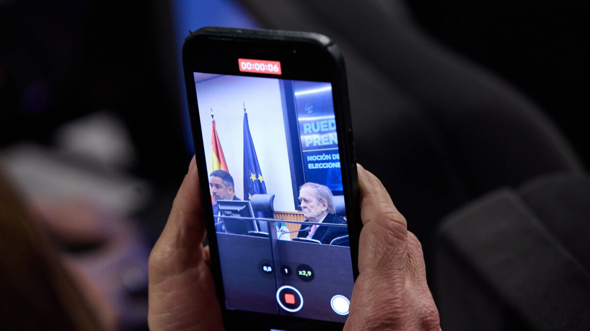 Una persona graba la comparecencia del presidente de VOX, Santiago Abascal (i), y el candidato de la moción de censura, el profesor Ramón Tamames (d), ante los medios en el Congreso de los Diputados