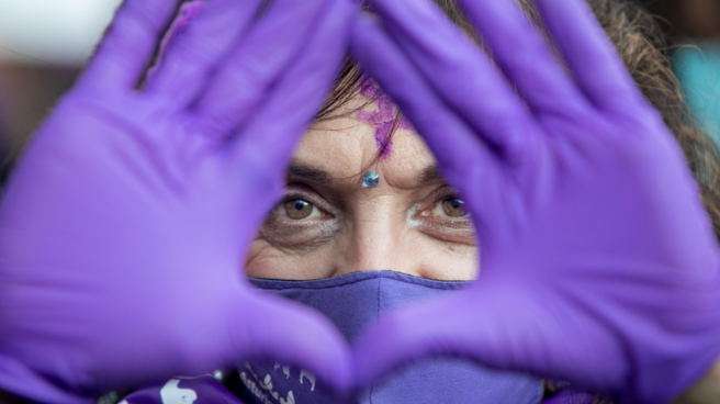 Mujer en una manifestación del 8M en España haciendo el símbolo del feminismo con las manos un día 8 de marzo