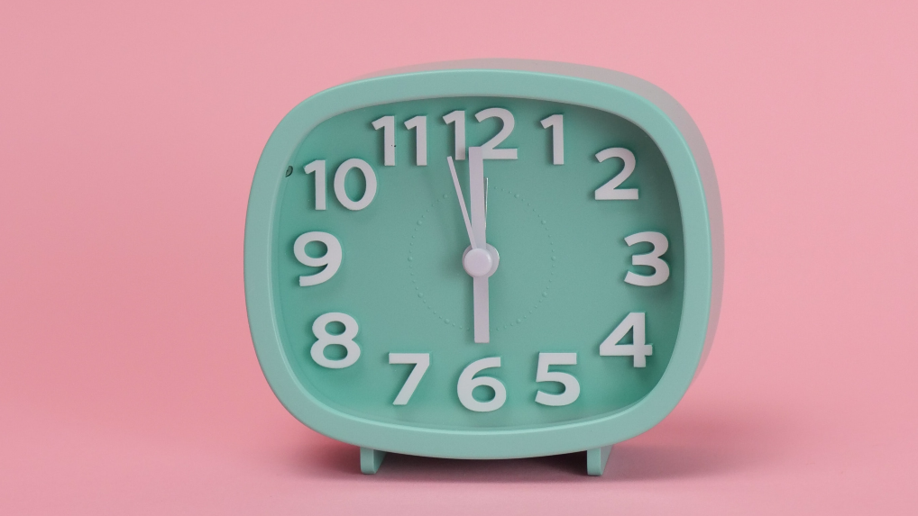 Reloj verde menta sobre fondo rosa que muestra el cambio de hora de marzo 2023 en España